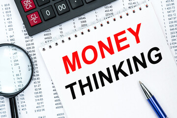 Fototapeta premium Text MONEY THINKING on financial tables with magnifying glass. Business and financial conzept. calculator, magnifying glass and the working paper with a diagram.
