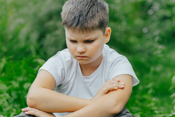 unhappy child covering her face with hands. crying boy sitting alone in park. Depression, stress,...