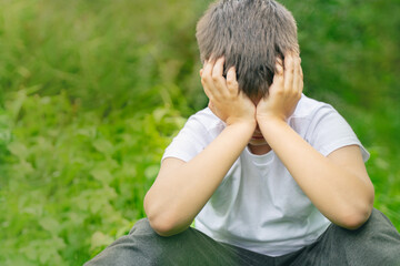 unhappy child covering her face with hands. crying boy sitting alone in park. Depression, stress,...