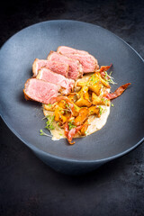 Modern style fried dry aged wagyu roast beef steak with chanterelle and bacon in cream sauce offered as close-up in a design plate