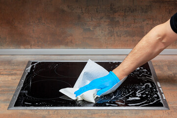 Adult man clean kitchen electric stove with a paper napkin and foam