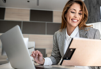 A young woman, alone in her office, enters data from her reminder into a laptop and smiles