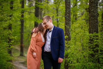 Romantic walk of a young couple in a green forest, warm spring weather. Guy and girl hugging in nature