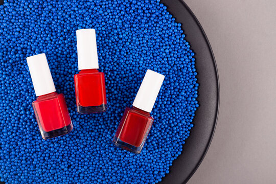 Three Red Nail Polish On Blue Background Of Plastic Texture Balls. High Quality Photo