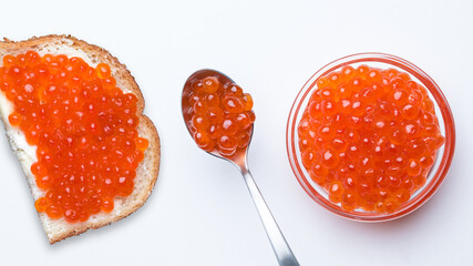 Salmon Red Caviar. Red fish caviar on a spoon in glass bowl. Sandwich with white bread, butter and red caviar. Raw seafood. Luxury food. White background. Flat lay, top view, copy space. 