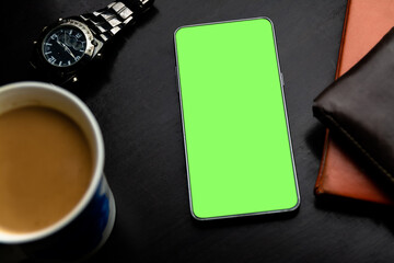 green screen smartphone on desk with coffee tea cup and wristwatch dark leather wallet and orange notebook organizer