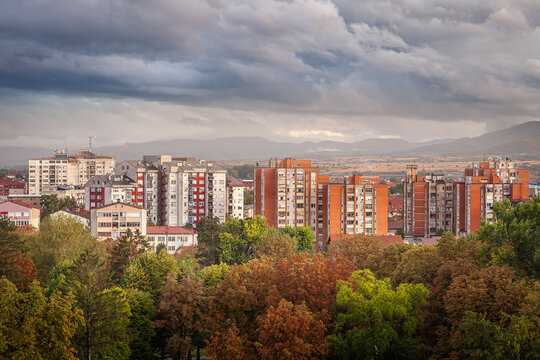 Autumn colors of foreground trees, doft light on old buildings and dramatic, blue hour sky above Pirot cityscape