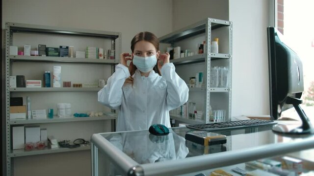 Caucasian girl, pharmacy worker shows how to properly put on a protective mask. Prerequisites for protecting against inhalation of the virus during the covid-19 pandemic. Drecautions at the drug store