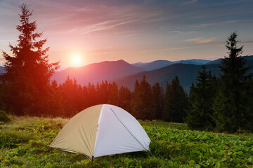 Summer landscape. Tourist tent in camp among meadow in the mountains at sunset. View of the dramatic evening sky. Red sunset and mountains in the background.