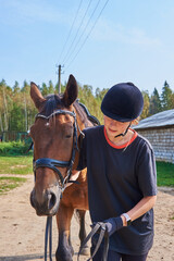 A girl leads a Bay horse on a warm early autumn day.