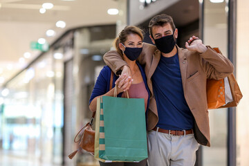 Young couple carries shopping bags and walks through the shopping mall, both wearing protective masks, life in a time of pandemic