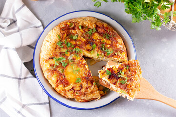 Potatoes and vegetables tortilla on a light background, top view. Potatoes, green beans, bell peppers, green peas, cheese, eggs casserole - delicious breakfast or snack