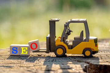 Yellow toy forklift hold letter block O to complete word SEO (Abbreviation of search engine optimization) on wood background