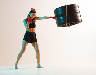 Cool female fighter trains jab on beige background in neon light. Women's sport and motivation...
