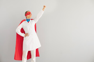 Fototapeta na wymiar Young doctor in superhero costume ready to fight diseases, grey background. Medical worker against infections