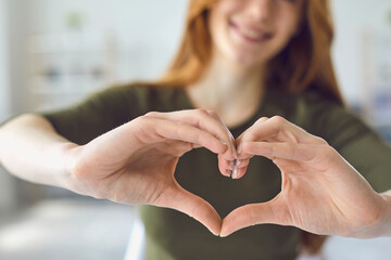 Close up of cute smiling teen girl gesture showing heart love symbol to camera.