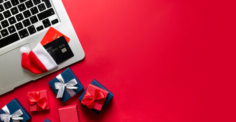 on a red banner background lie a computer laptop laptop bank credit cards in a santa hat and gifts in boxes with bows of red and blue colors