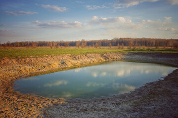 A small drying pond in the evening in the field. Cloudy sky over the lake. Landscape.