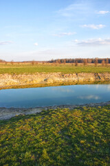A small drying pond in the evening in the field. Cloudy sky over the lake. Landscape.