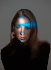 Creative portrait of stylish young woman with blue neon light on face and perfect skin on gray background