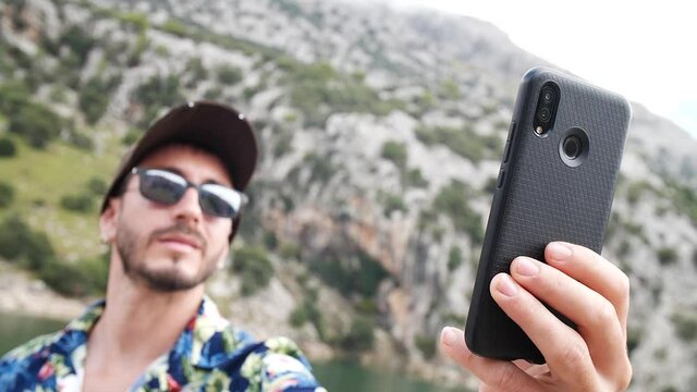 Man modeling with hawaiian shirt, taking a selfie in beautiful sunny day with mountain scenery in the back, Gorg blau lookout, Mallorca island, Spain.
Mid angle, traveling + parallax movements, slow m