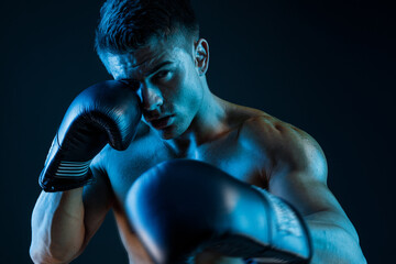 Muscular model sports young man in boxing gloves on dark background. Sexy torso. Male flexing his...