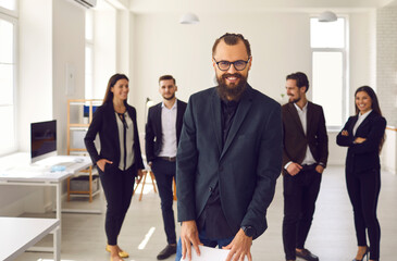 Cheerful young businessman with group of employees smiling and looking at camera