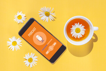 Smartphone with podcast, cup of tea and chamomile flowers on a bright yellow background. Copyspace,...
