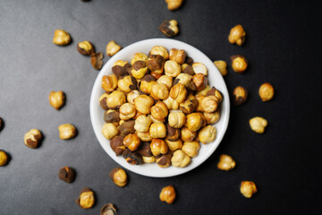 Top view of roasted chickpeas in white bowl on black textured background
