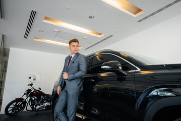 A young businessman looks at a new car in a car dealership. Buying a car