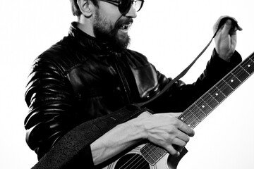 A man plays the guitar in a black leather jacket with sunglasses on a light background