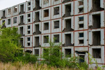 An abandoned multi-storey building stands in the middle of a green field. Multi-storey building without windows