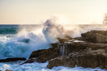 Fototapeta na wymiar Große Welle prallt gegen den Felsen einer Küste im Sonnenlicht