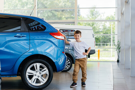 At a car dealership, a happy boy stands near a new car before buying it. Car purchase
