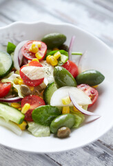 Simple Salad with Green Olives, Cucumber, Cherry Tomatoes and Capers. Bright wooden background. Close up.