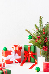 Fototapeta na wymiar Red and green gift boxes and balls with candles , fir tree branches and hawthorn twigs in a vase on white wall background, new year and christmas concept