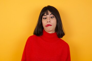 Caucasian brunette woman wearing red casual sweater isolated over yellow background  showing grimace face crossing her eyes and showing tongue . Being funny and crazy