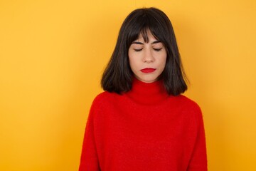 Caucasian brunette woman wearing red casual sweater isolated over yellow background  looking sleepy and tired, exhausted for fatigue and hangover, lazy eyes in the morning.