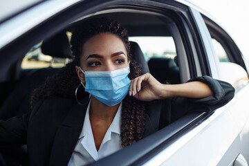 Young business woman fixing and adjusting her medical mask while sitiing in the car behind the steering wheel. Business trips during pandemic, new normal and coronavirus travel safety concept.