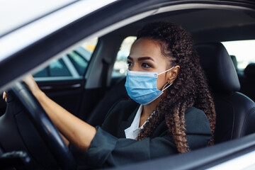 Young woman taxi driver sits in a car behind the steering wheel and driving during the covid-19 quarantine. Business trips during pandemic, new normal and coronavirus travel safety concept.