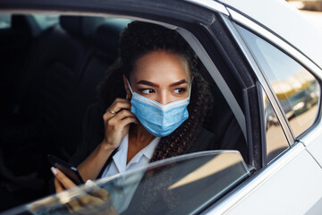 Woman wearing a medical mask on a business travel around the city checking her mobile phone,...