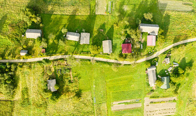 Birds eye view of group old wooden huts on mountain slope. Dirt road passes between them. Countryside, top view