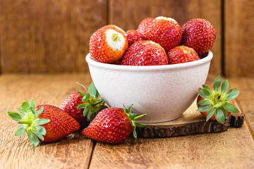 organic and fresh strawberries in recycled plastic bowl on rustic wooden background with space for text