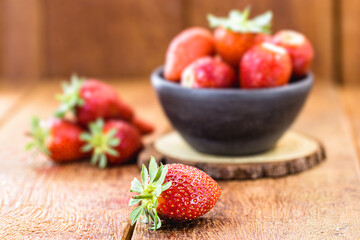 fresh strawberries on rustic wooden background, in handmade clay bowl, space for text