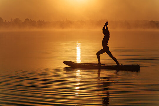 Silhouette Of Sportive Man Doing Yoga On Paddle Board