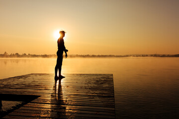 Sporty man in silhouette relaxing on pier after morning swim