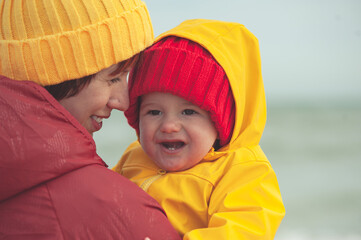 Young happy mother with a baby on the seashore in colorful clothes.