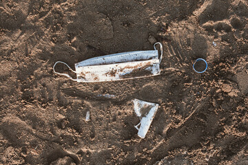 Plastic trash, dirty sandy beach. Medical mask on the sand.  Pollution due to coronavirus. Single-Use Plastic. Covid-19.