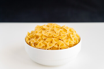 Raw dry uncooked Farfalle pasta spaghetti noodle on white bowl wooden background for basil tomato pesto sauce Homemade Italian food organic whole wheat vegan spaghetti for a healthy meal
