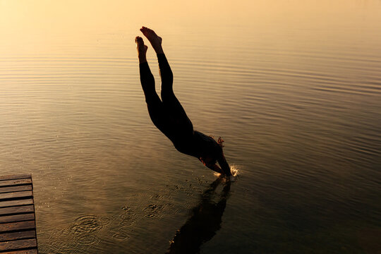 Strong muscular guy plunge into water from wooden pier